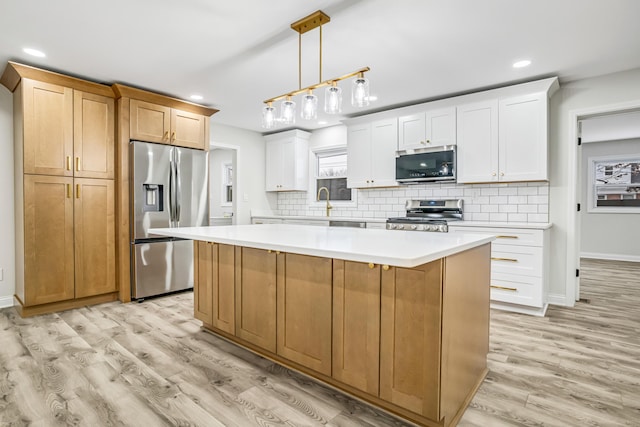 kitchen featuring pendant lighting, appliances with stainless steel finishes, light hardwood / wood-style floors, white cabinets, and a kitchen island