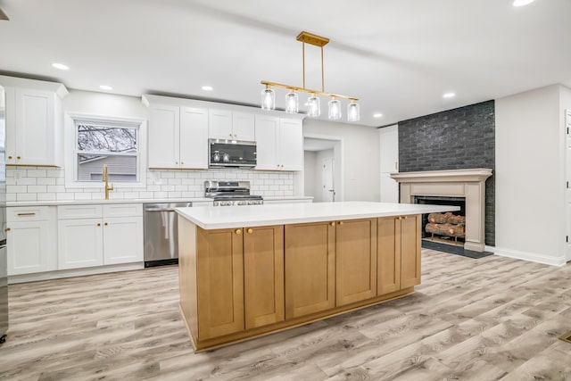 kitchen featuring white cabinetry, decorative light fixtures, a kitchen island, and appliances with stainless steel finishes