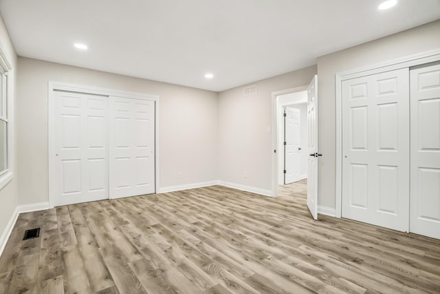 unfurnished bedroom featuring light hardwood / wood-style flooring and two closets