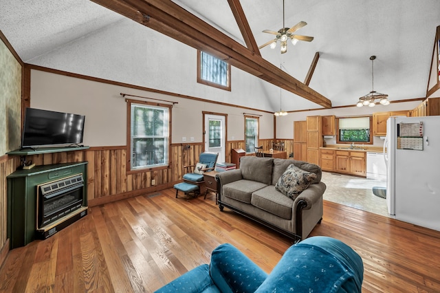 living area featuring a wainscoted wall, ceiling fan with notable chandelier, light wood-style floors, and beamed ceiling