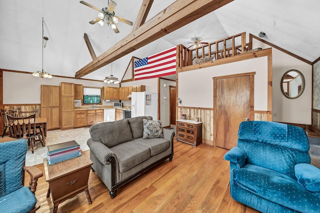 living room with wainscoting, high vaulted ceiling, light wood-type flooring, beamed ceiling, and ceiling fan with notable chandelier