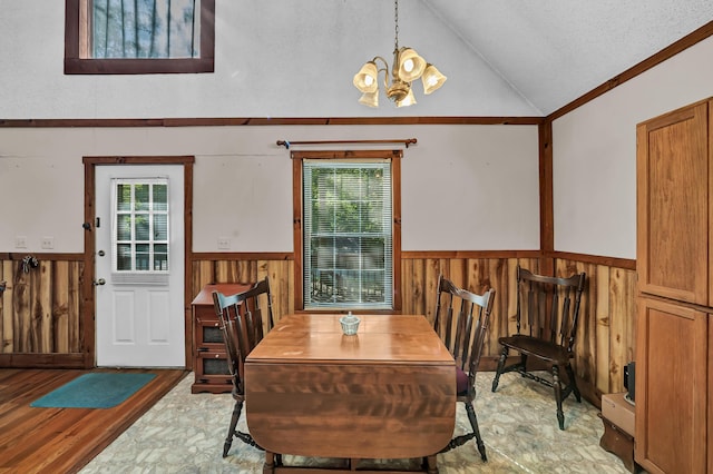 dining space with a wainscoted wall, wooden walls, a textured ceiling, a chandelier, and light wood-type flooring