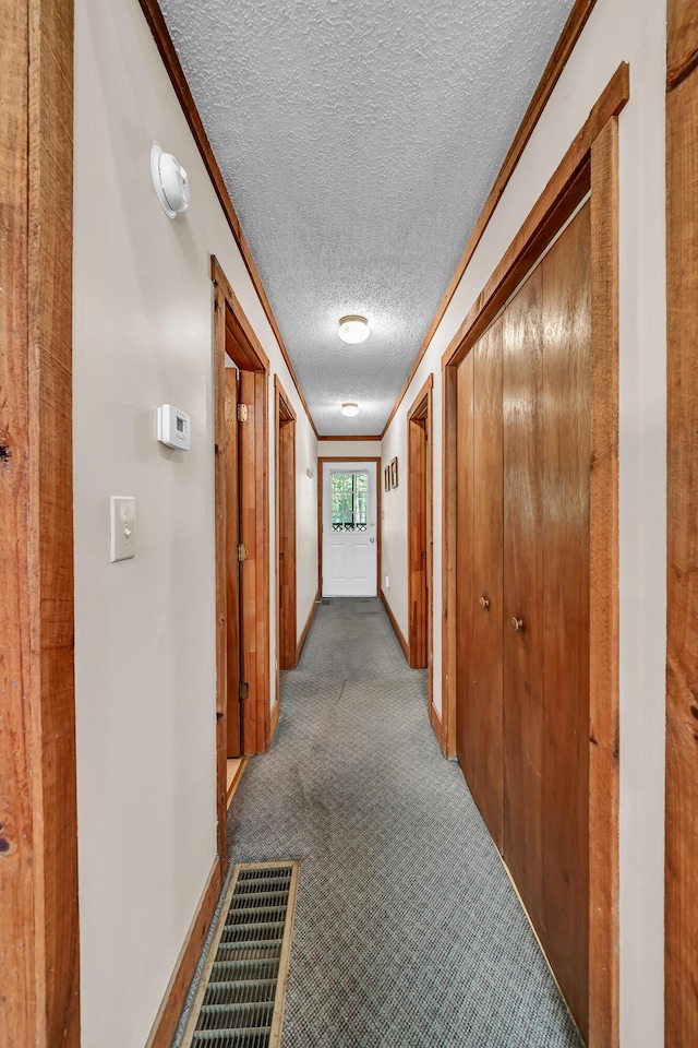 corridor with a textured ceiling, visible vents, baseboards, ornamental molding, and carpet