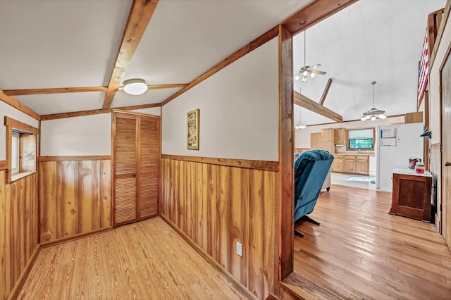 home office featuring lofted ceiling with beams, wooden walls, a wainscoted wall, a ceiling fan, and light wood finished floors