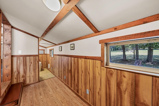 spare room featuring lofted ceiling with beams, light wood-style floors, wooden walls, and wainscoting