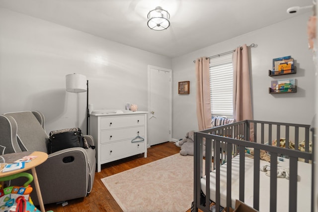 bedroom with dark wood-type flooring and a crib