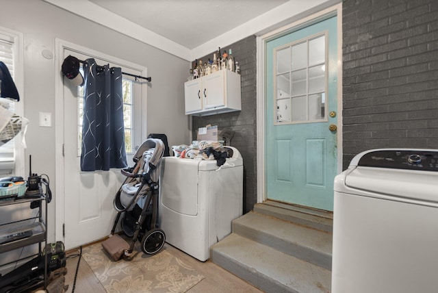 clothes washing area featuring light hardwood / wood-style flooring, cabinets, and brick wall