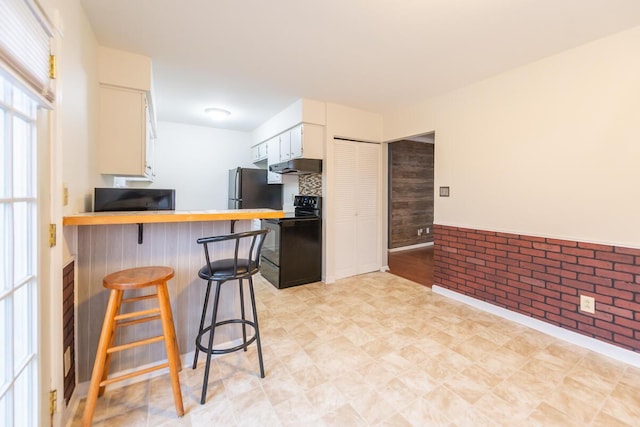 kitchen with brick wall, a breakfast bar area, white cabinets, electric range, and kitchen peninsula