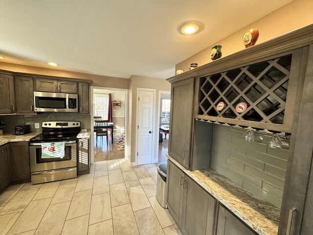 kitchen with appliances with stainless steel finishes, light stone countertops, dark brown cabinets, and backsplash