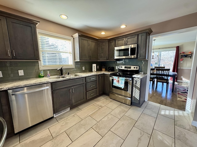 kitchen with sink, backsplash, dark brown cabinets, stainless steel appliances, and light stone countertops