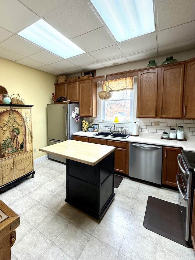 kitchen featuring appliances with stainless steel finishes, a paneled ceiling, tasteful backsplash, butcher block counters, and sink