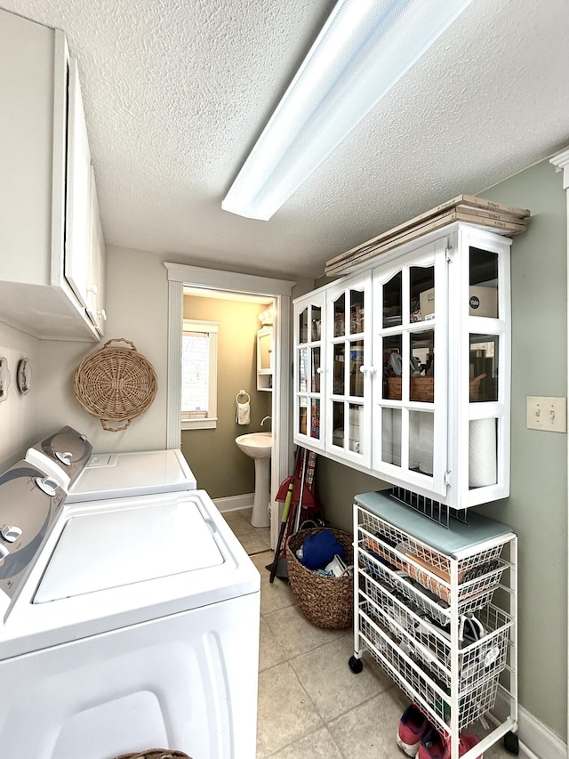 laundry area with sink, washing machine and dryer, cabinets, a textured ceiling, and light tile patterned flooring