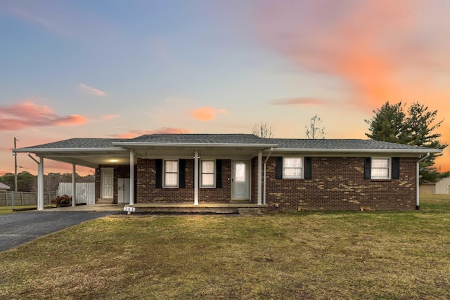 single story home featuring brick siding, a lawn, fence, a carport, and driveway