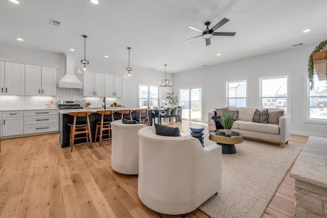 living room featuring ceiling fan with notable chandelier and light hardwood / wood-style flooring