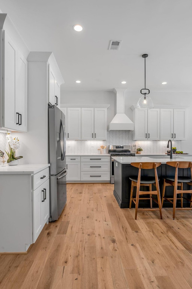 kitchen with a kitchen bar, hanging light fixtures, appliances with stainless steel finishes, custom range hood, and white cabinets