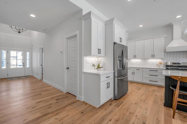 kitchen with white cabinetry, stainless steel appliances, wall chimney exhaust hood, and light hardwood / wood-style flooring