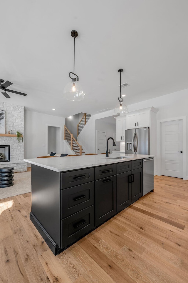 kitchen featuring hanging light fixtures, stainless steel appliances, an island with sink, and white cabinets