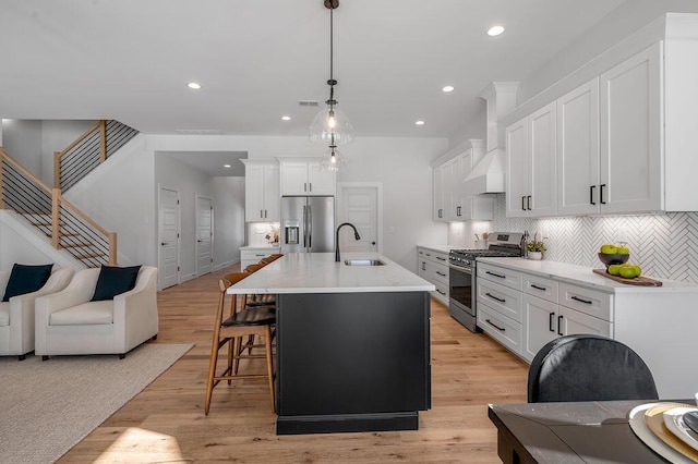 kitchen featuring pendant lighting, sink, white cabinetry, stainless steel appliances, and an island with sink