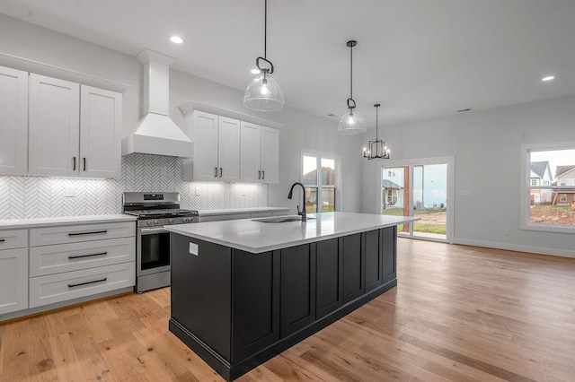 kitchen with premium range hood, white cabinetry, stainless steel range with gas cooktop, and sink