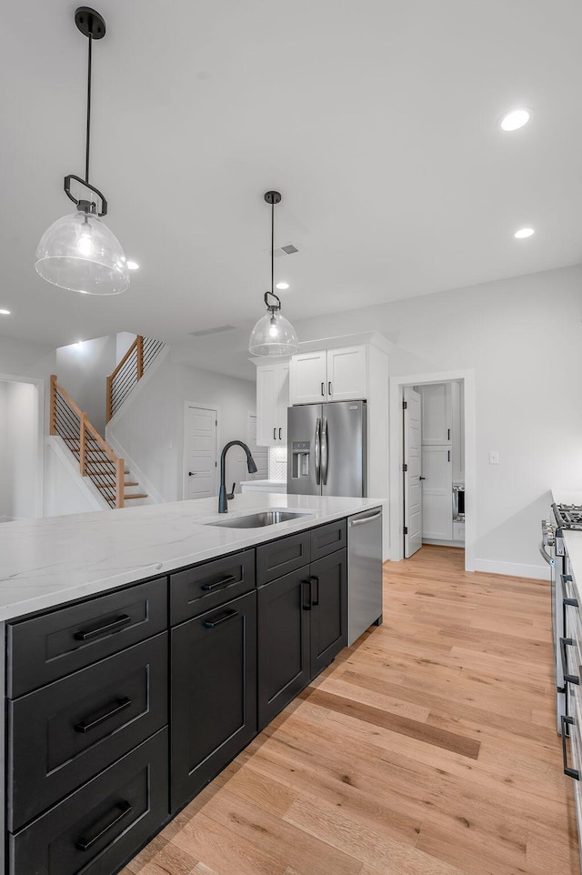 kitchen featuring pendant lighting, white cabinetry, sink, stainless steel appliances, and light hardwood / wood-style flooring