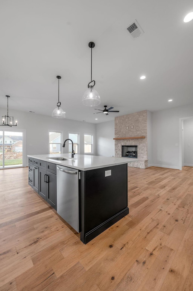 kitchen featuring pendant lighting, stainless steel dishwasher, sink, and a kitchen island with sink