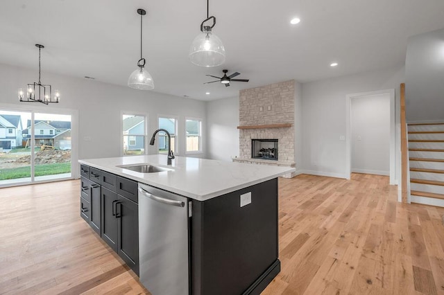 kitchen with sink, a kitchen island with sink, decorative light fixtures, stainless steel dishwasher, and light wood-type flooring