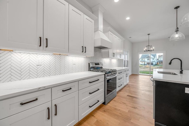 kitchen with sink, stainless steel gas range, hanging light fixtures, white cabinets, and custom exhaust hood