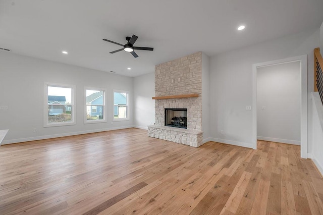 unfurnished living room featuring ceiling fan, a stone fireplace, and light hardwood / wood-style floors