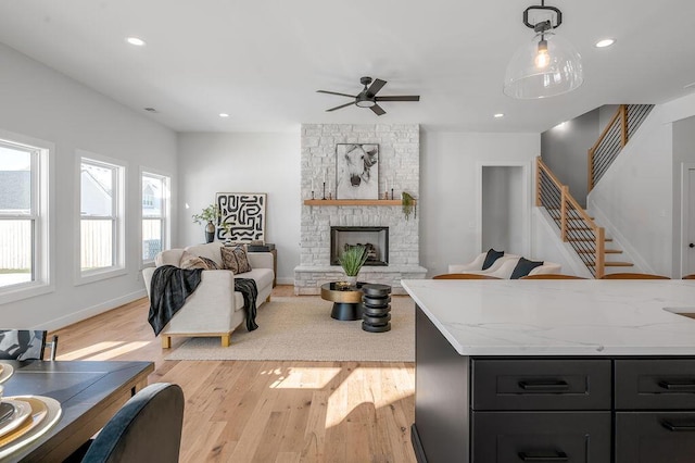 living room featuring a stone fireplace, ceiling fan, and light wood-type flooring