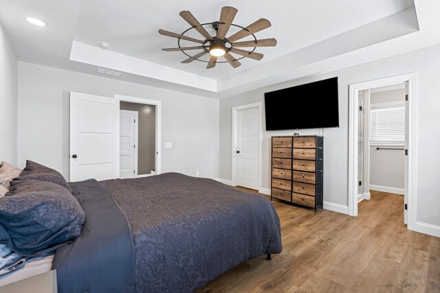 bedroom with a tray ceiling, wood finished floors, and baseboards