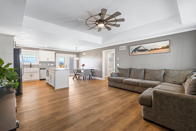 living room featuring a raised ceiling, visible vents, light wood-style floors, ornamental molding, and baseboards