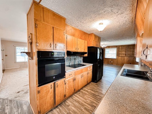 kitchen featuring sink, black appliances, light hardwood / wood-style floors, a textured ceiling, and wood walls