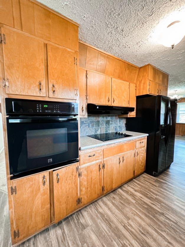 kitchen featuring a textured ceiling, decorative backsplash, light hardwood / wood-style floors, and black appliances