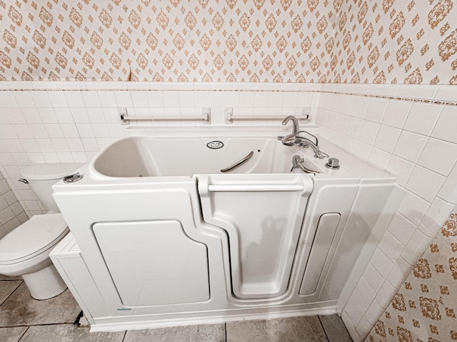 bathroom with tile patterned flooring, tile walls, a bathtub, and toilet