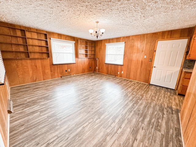 spare room featuring hardwood / wood-style flooring, wooden walls, an inviting chandelier, and a textured ceiling