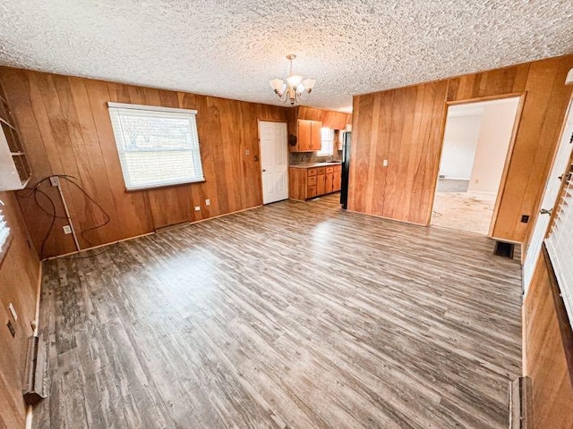 unfurnished living room featuring hardwood / wood-style flooring, wooden walls, an inviting chandelier, and a textured ceiling