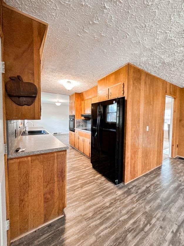 kitchen with sink, wooden walls, black appliances, a textured ceiling, and light wood-type flooring