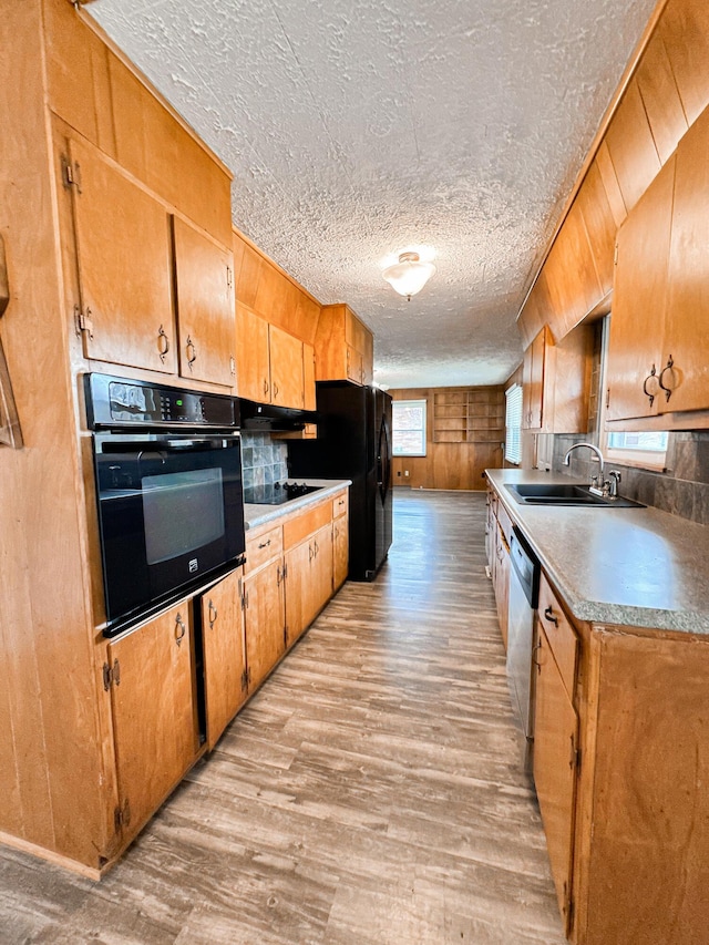 kitchen with wooden walls, sink, light hardwood / wood-style floors, black appliances, and a textured ceiling