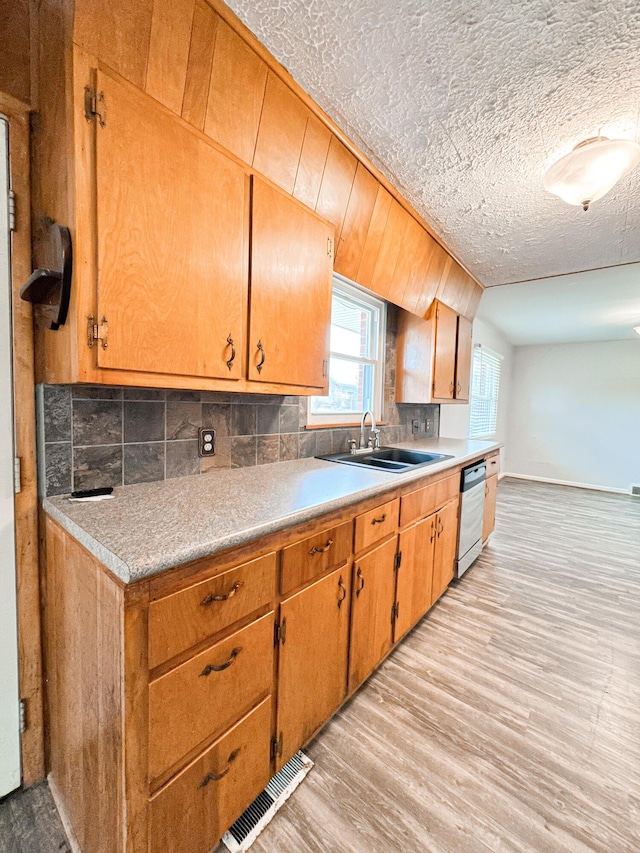 kitchen featuring sink, tasteful backsplash, light hardwood / wood-style flooring, a textured ceiling, and dishwasher