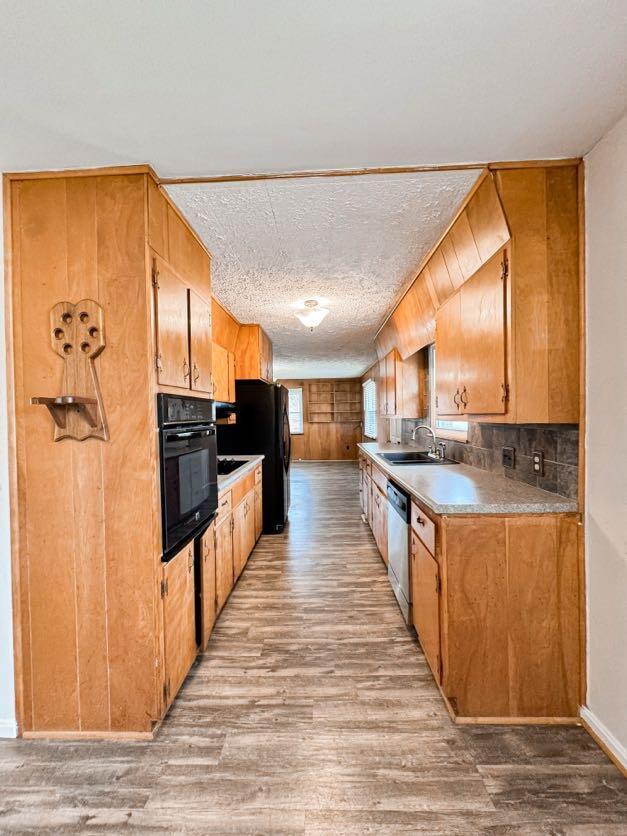 kitchen with sink, light hardwood / wood-style flooring, a textured ceiling, and black appliances