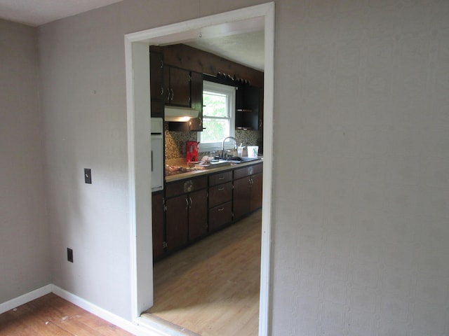 kitchen featuring dark brown cabinetry, sink, light wood-type flooring, black electric stovetop, and oven