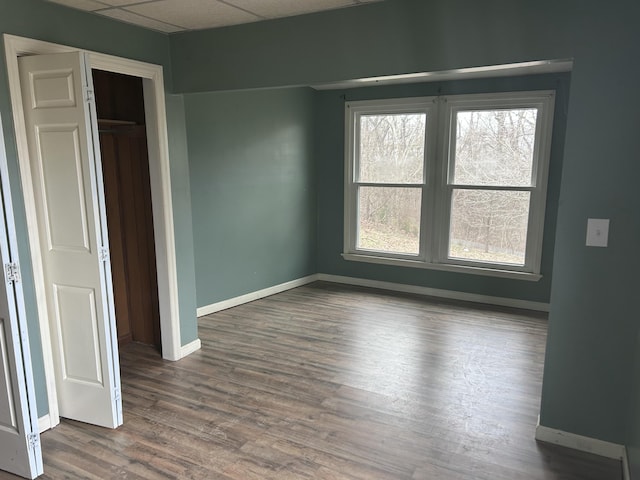 unfurnished bedroom with multiple windows, hardwood / wood-style floors, a drop ceiling, and a closet