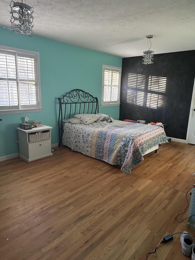 bedroom with a notable chandelier, a textured ceiling, and hardwood / wood-style floors