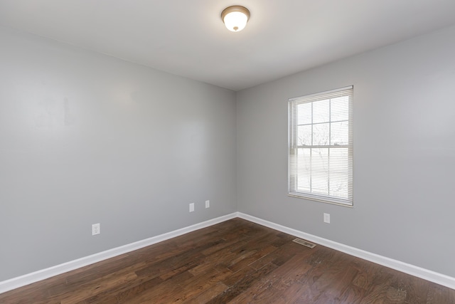 unfurnished room featuring dark wood-type flooring, visible vents, and baseboards