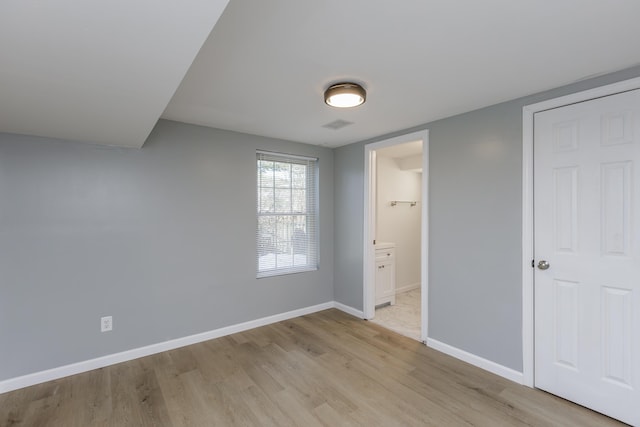 unfurnished bedroom with light wood finished floors, ensuite bath, and baseboards