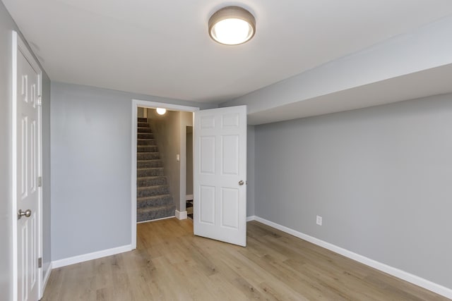 finished basement featuring stairway, light wood-style flooring, and baseboards