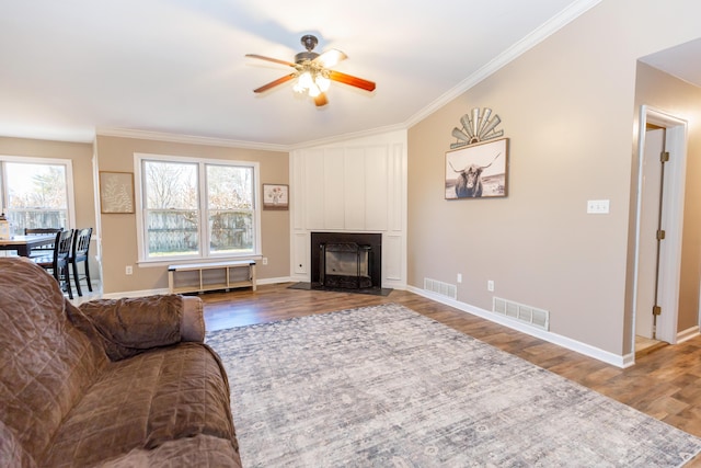 living area with ornamental molding, a large fireplace, visible vents, and wood finished floors