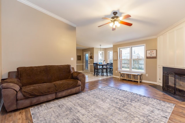 living room featuring ceiling fan, a large fireplace, baseboards, dark wood-style floors, and crown molding