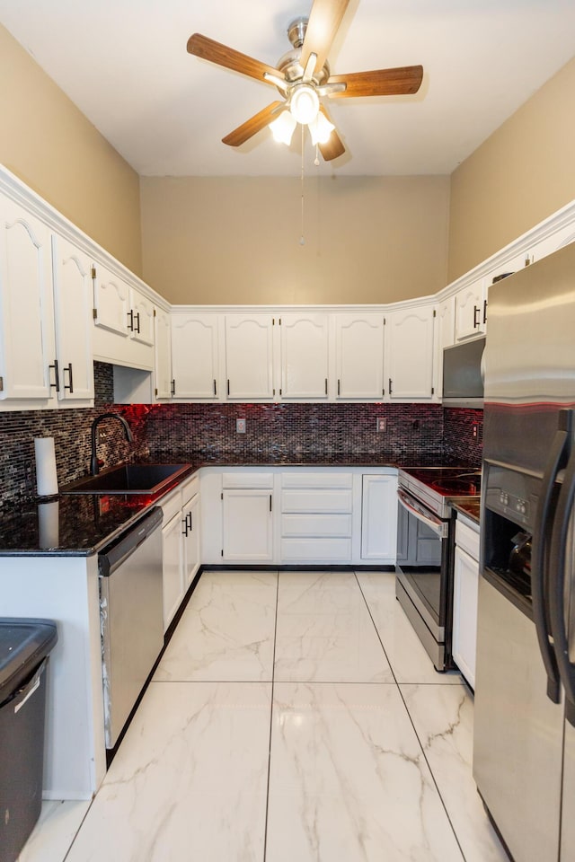 kitchen featuring white cabinets, a sink, stainless steel appliances, and dark stone countertops