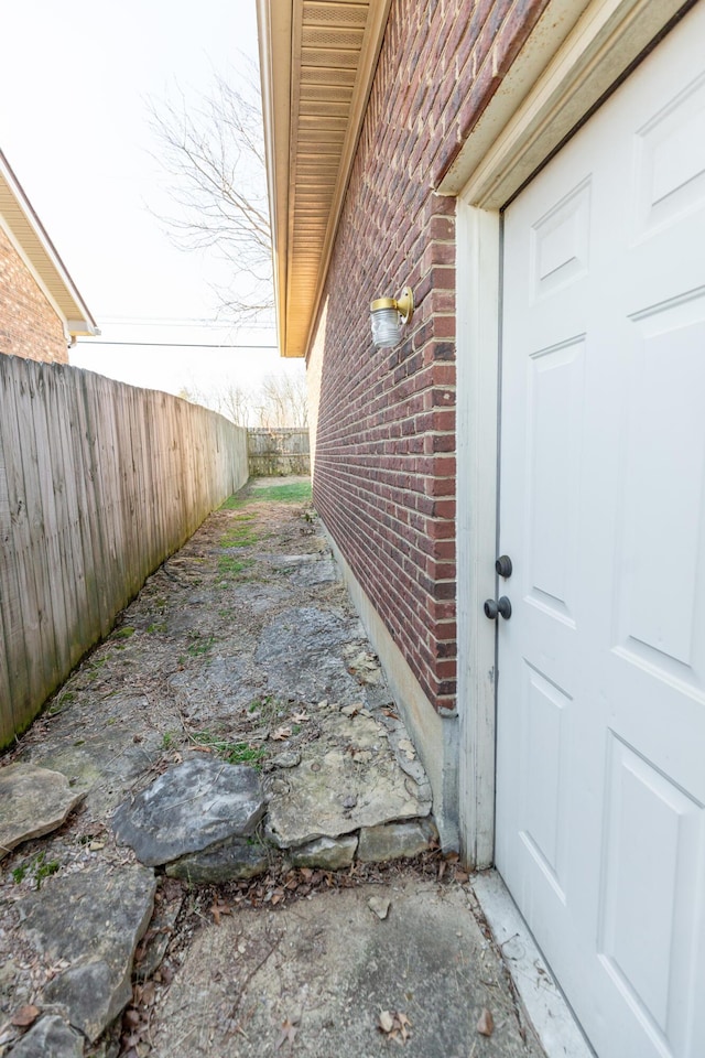 property entrance with a garage, fence, and brick siding